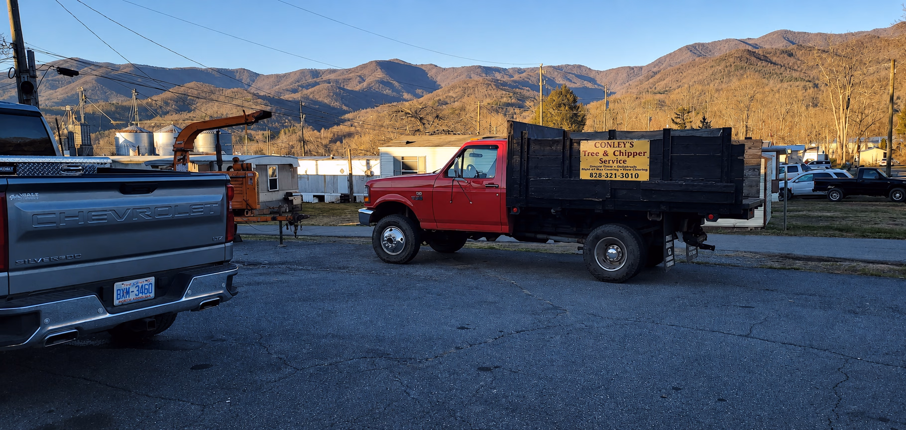 Red truck with black sides and sign for Conley's Tree & Chipper Service parked on asphalt with mountains in background.