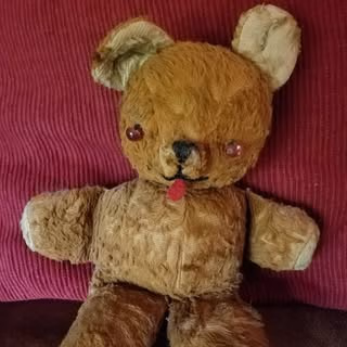Worn brown teddy bear with a red tongue on a pink textured fabric background.