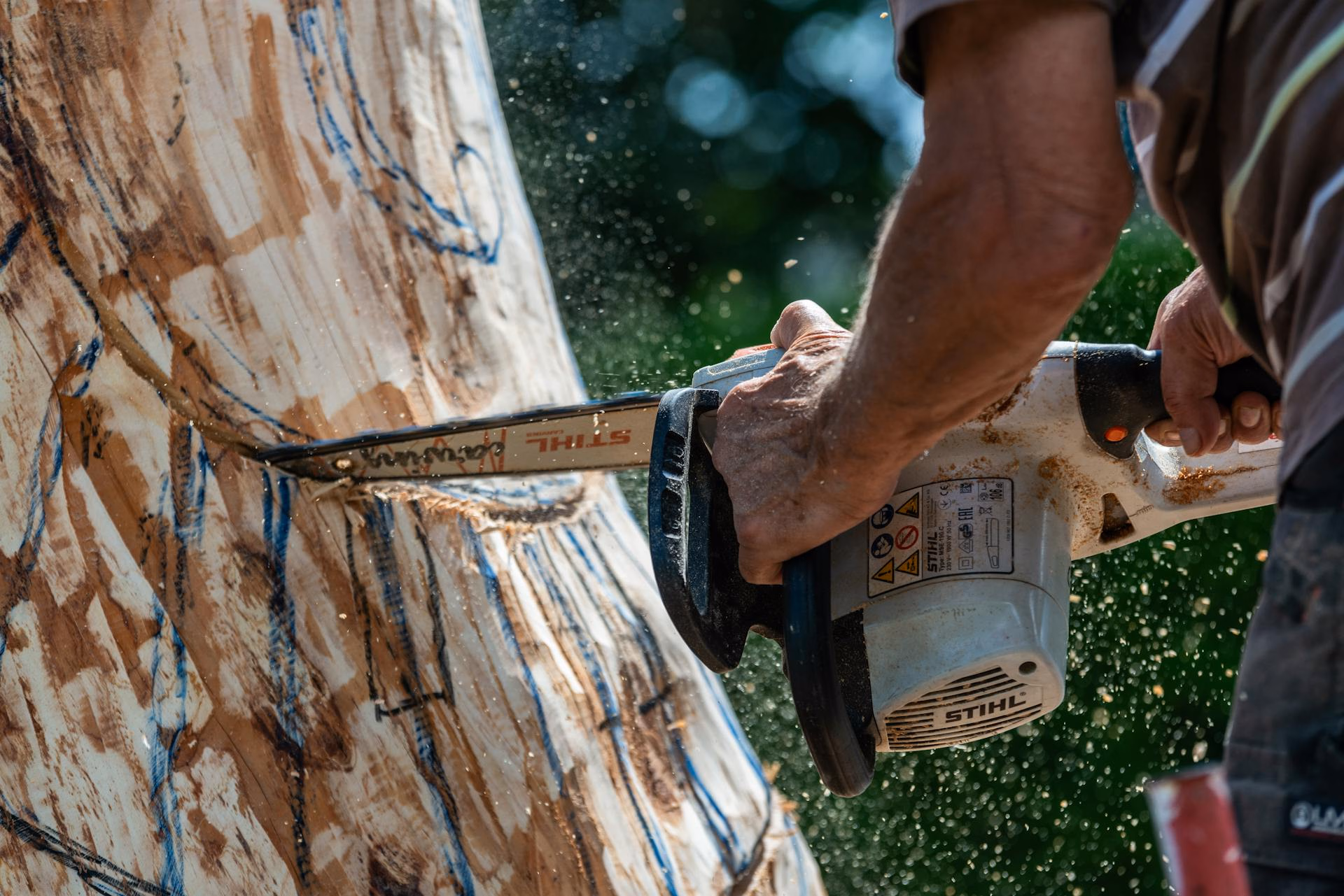 Person using a Stihl chainsaw to carve a large log during woodwork outdoors.